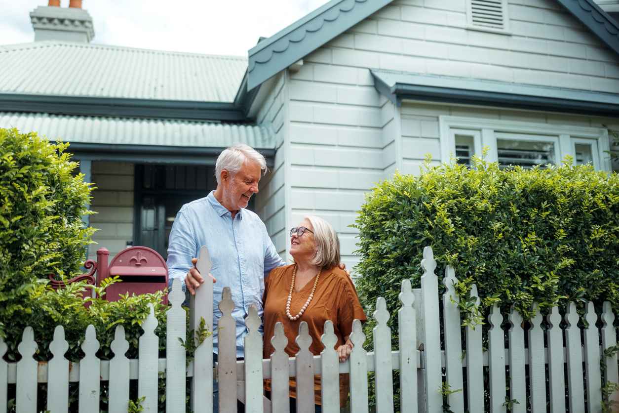 Senior couple bonding while standing near fence in their front yard